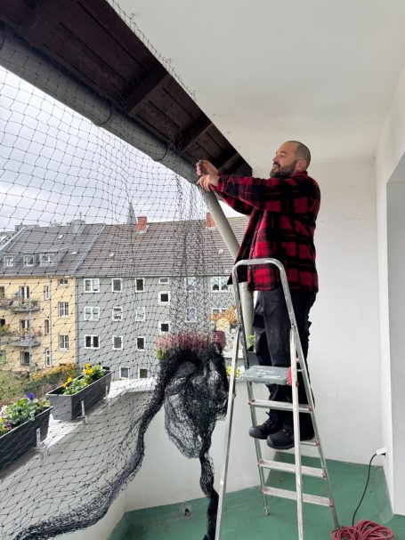 Handwerker befestigt Katzennetz am Balkon an zuvor montierten Haken